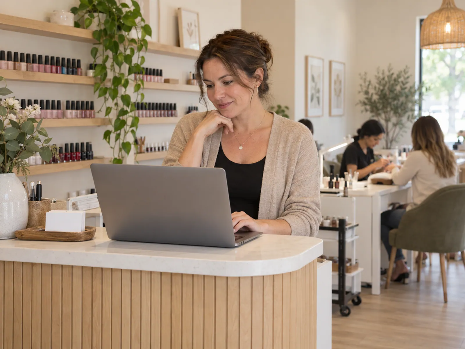 A nail salon owner reviewing work on a laptop at the reception desk.